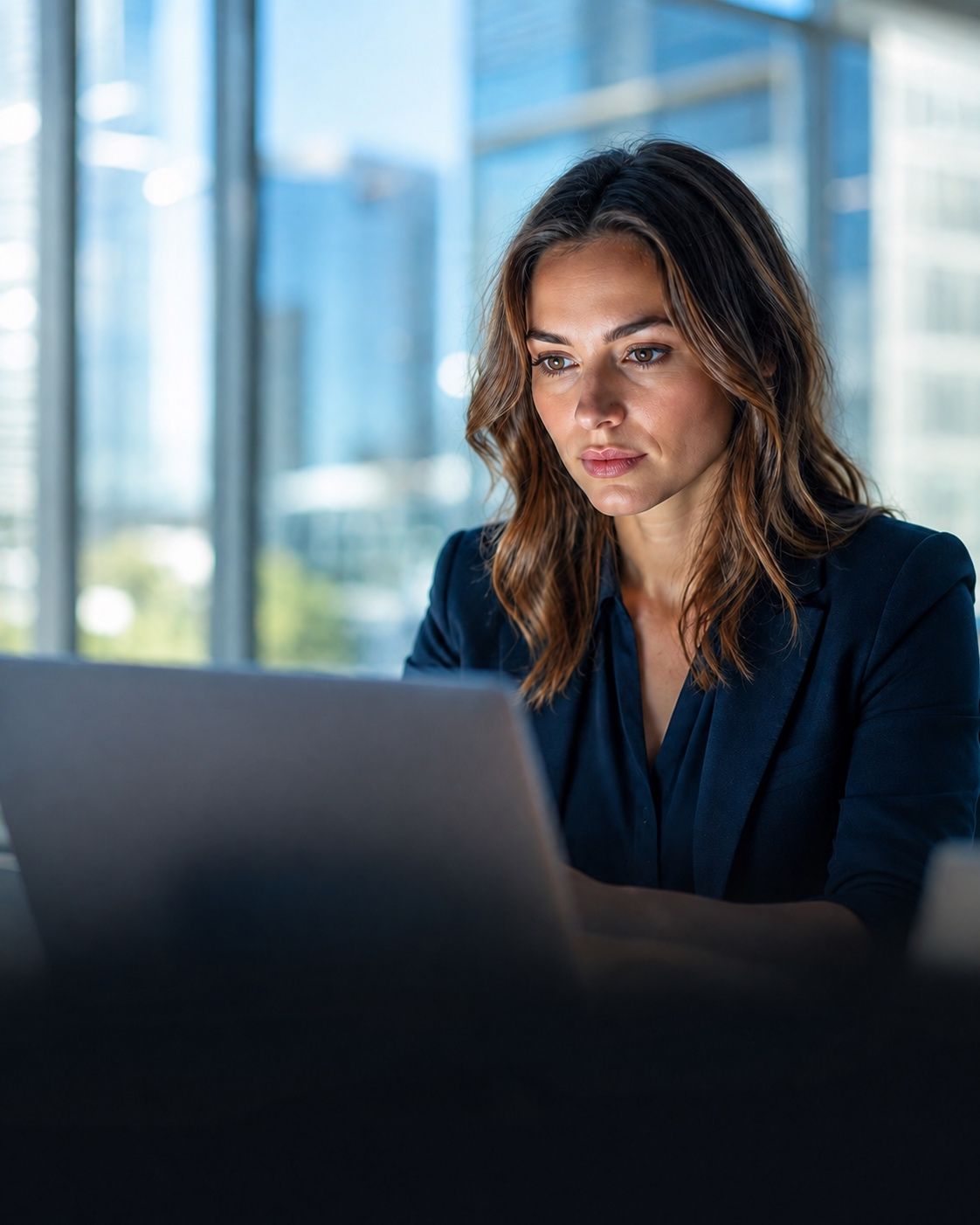 A professional at a laptop in a sunlit office with softly blurred windows behind her
