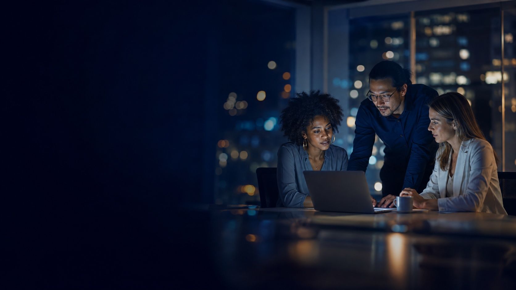 Professionals collaborating in a glass-walled office with softly glowing city lights
